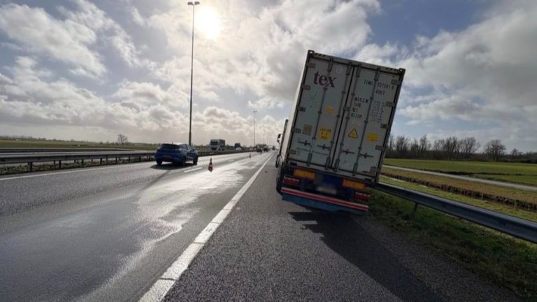 Lange file door vrachtwagen die scheef in de berm staat, vangrails houdt hem nog net tegen